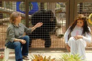 Na frente da jaula de Bubbles, a instrutora do santuário para símios explica para La Toya a rotina do animal. - QUEEN