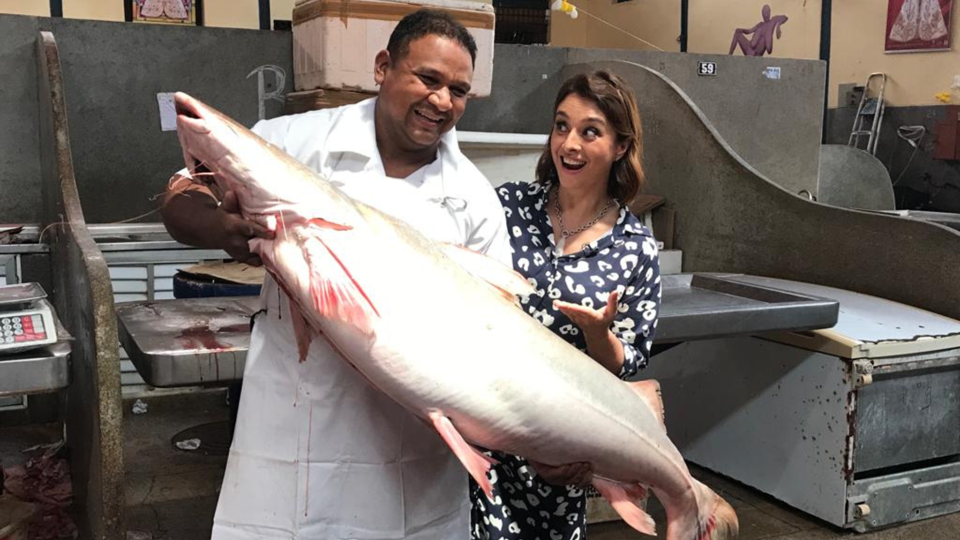 Catia ao lado de peixeiro, segurando peixe gigante