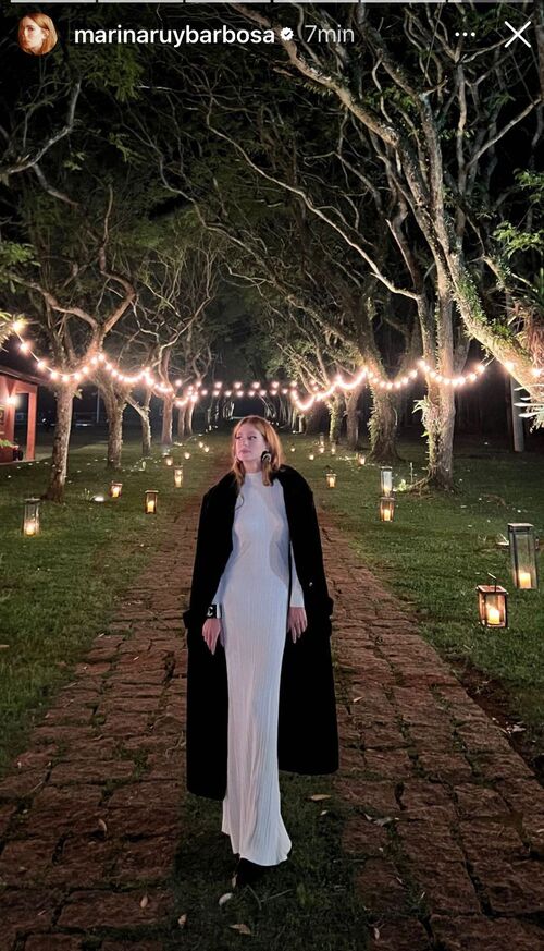 a atriz usando um vestido longo cor azul-bebê e vestindo um sobretudo preto por cima da peça. 