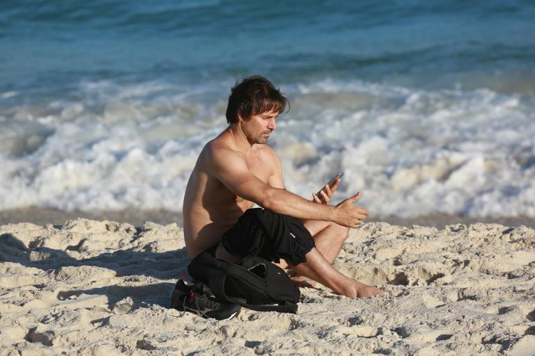 Sem desgrudar do celular, Murilo Rosa curte dia de praia no Rio de Janeiro