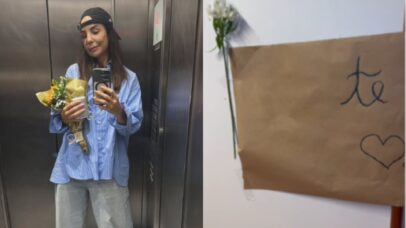 Mulher em elevador com buquê de flores e celular na mão, ao lado de um bilhete com 'te amo' escrito.