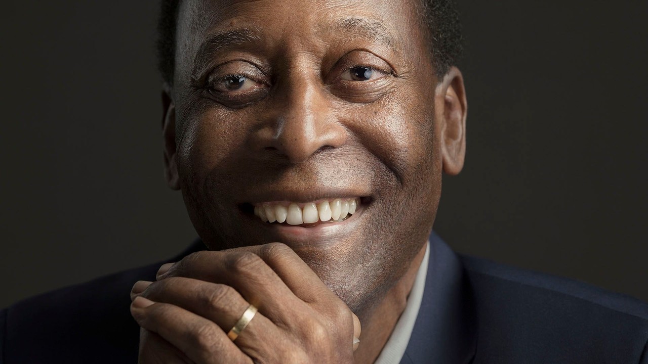 Pelé sorrindo em close-up, usando blazer azul, camisa branca e anel dourado