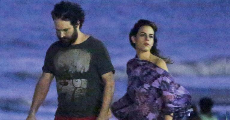 Caco Ciocler e Luisa Micheletti caminham de noite na praia da Barra no Rio de Janeiro