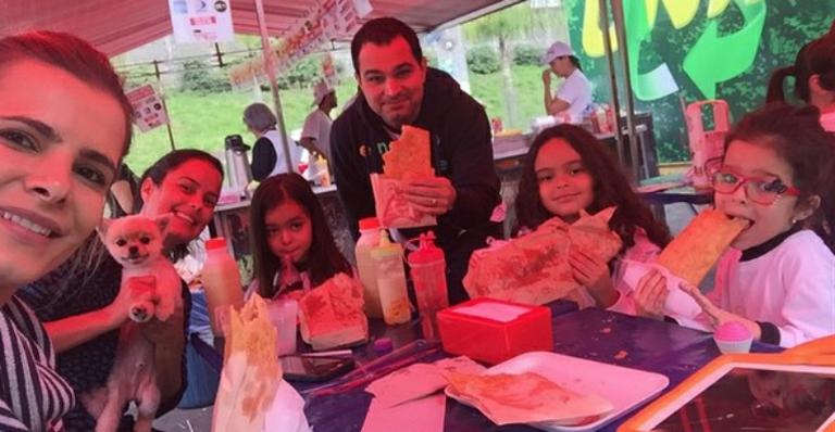 Luciano come pastel em feira com as filhas e a mulher