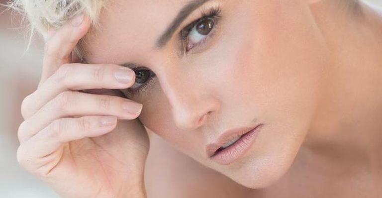 Sem sutiã, Deborah Secco aparece apenas com um casaco branco e deixa seios aparecerem